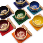 Top view of all 7 singing bowls and sticks, stood on their mats, showing chakra symbol decorations within the bowls.